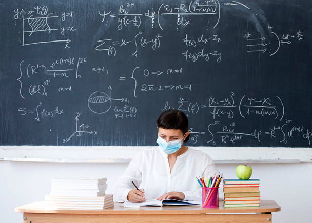 Female teacher with mask teaching math lesson at school. Social distanting and classroom safety during coronavirus epidemic - 写真・画像