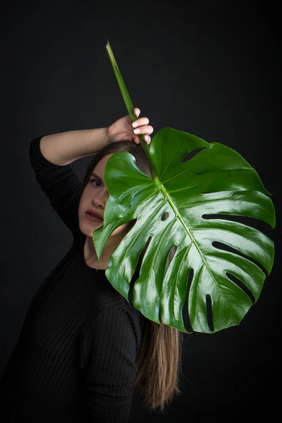 Portrait of beautiful woman with green tropical leaf on black backdrop - Fotó, kép
