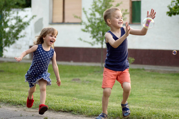 Játékos futó boldog gyerekek, hat éves fiú és három éves lány játszanak a szabadban, gondtalan vidám gyermekkor. - Fotó, kép