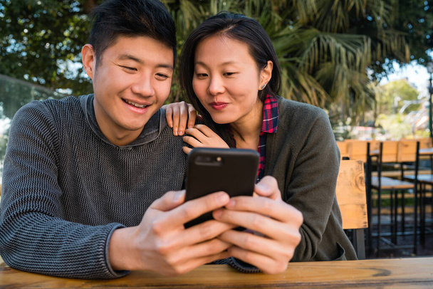 Portrait of lovely asian couple looking at the mobile phone while sitting and spending time at the coffee shop. Love and technology concept. - 写真・画像