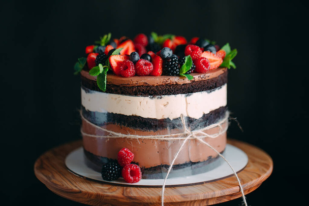 Fruit cake. Cake decorated with berries on a wooden stand on a black background. - Photo, image