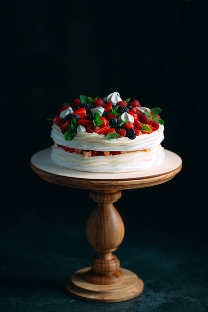 Fruit cake. Cake decorated with berries on a wooden stand on a black background. - Fotoğraf, Görsel