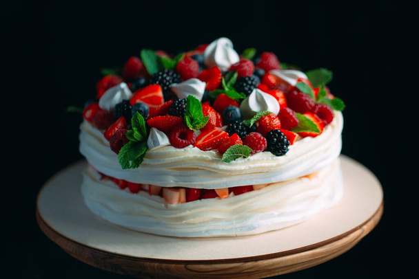 Fruit cake. Cake decorated with berries on a wooden stand on a black background. - Foto, Bild