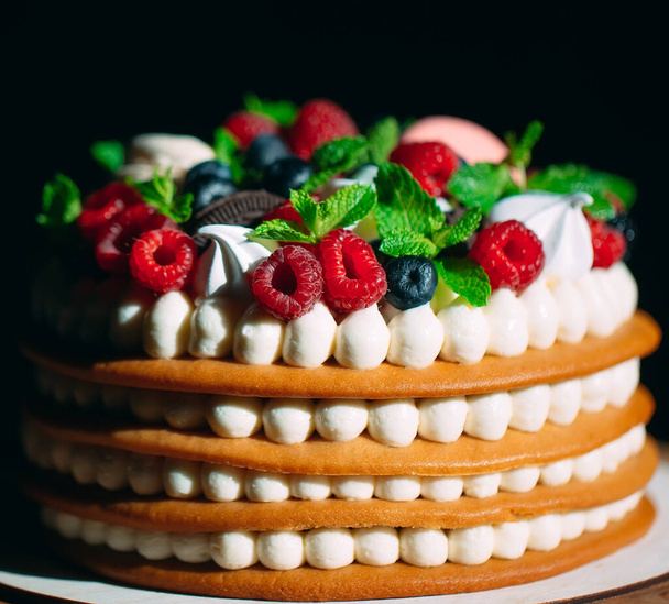 Fruit cake. Cake decorated with berries on a wooden stand on a black background. - Foto, immagini