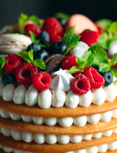 Fruit cake. Cake decorated with berries on a wooden stand on a black background. - 写真・画像