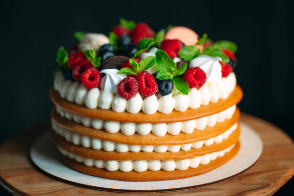 Fruit cake. Cake decorated with berries on a wooden stand on a black background. - Foto, immagini