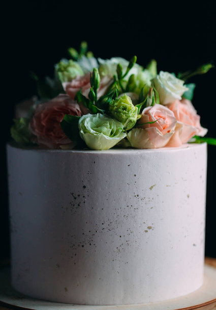 Η τούρτα είναι διακοσμημένη με λουλούδια σε σκούρο φόντο. - Φωτογραφία, εικόνα