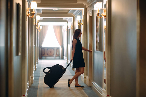 Young woman with handbag and suitcase in an elegant suit walks the hotel corridor to her room. - Foto, afbeelding