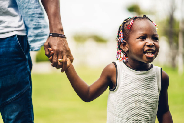Πορτρέτο του απολαύσετε ευτυχισμένη αγάπη μαύρο οικογένεια αφροαμερικανός πατέρας κρατώντας μικρό αφρικανικό κορίτσι χέρι σε στιγμές διασκέδασης στο πάρκο καλοκαίρι στο σπίτι - Φωτογραφία, εικόνα