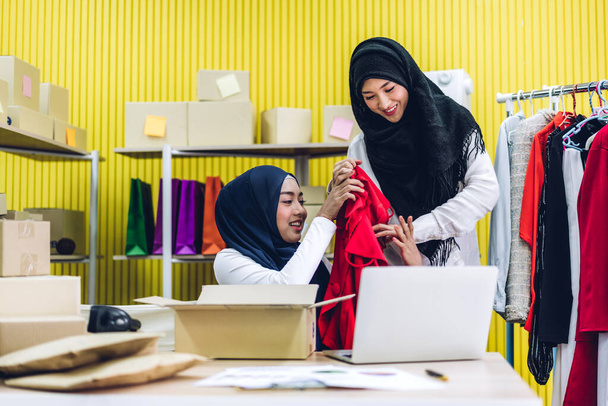 Portrait de sourire beau deux musulman propriétaire asiatique femme freelancer sme entreprise achats en ligne de travail sur ordinateur portable avec boîte de colis sur la table à la maison - Business expédition et livraison en ligne - Photo, image