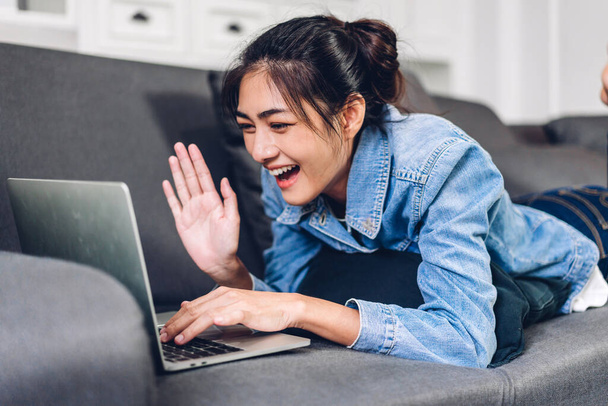 Jonge Aziatische vrouw ontspannen met behulp van laptop computer werken en video conferentie vergadering thuis.Jonge creatieve meisje zeggen hallo en typen op toetsenbord.work vanuit huis concept - Foto, afbeelding