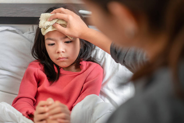 Asian mother take cool towel for reduce high fever on sick girl forehead on bed at morning time, Selective focus, Healthy and infection concept - Fotó, kép