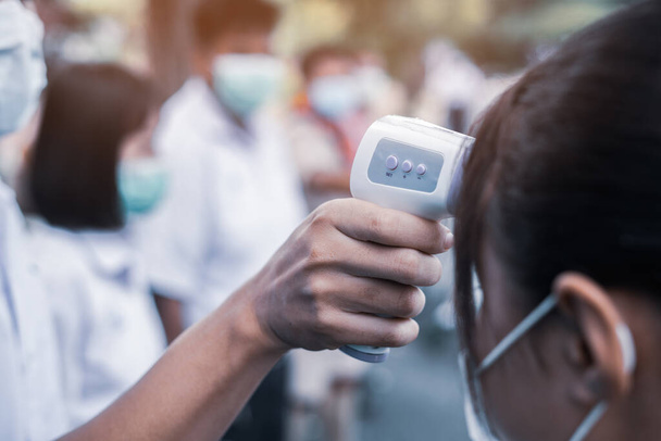 Hand houden infrarood thermometer pistool voorhoofd temperatuur test om student te controleren op virus covid-19 symptomen te beschermen in de school - Foto, afbeelding