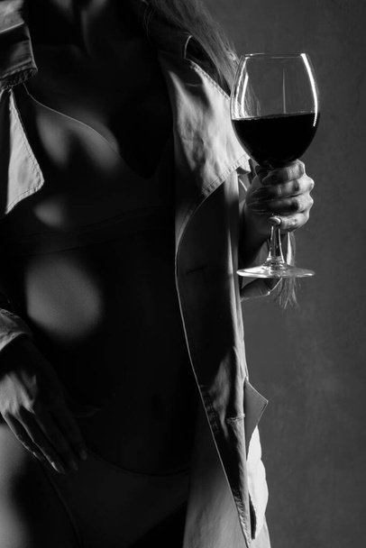 Copa de vino tinto. mujer joven con una copa de vino, enfoque selectivo. Mujer sexy con lencería y abrigo. Monocromo - Foto, Imagen