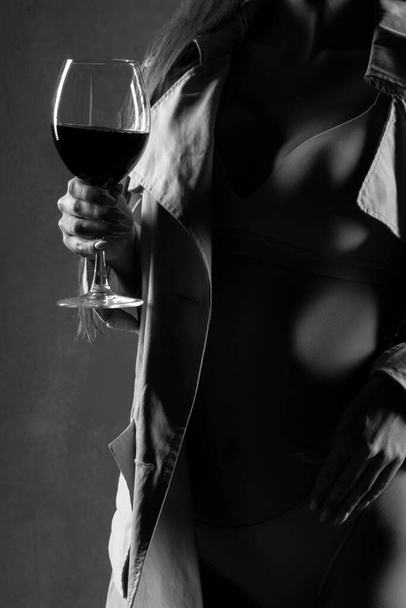 Red wine glass. young woman with a glass of wine, selective focus. Sexy woman wearing lingerie and coat. Monochrome - Photo, Image