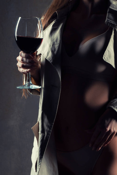Бокал красного вина. молодая женщина с бокалом вина, избирательный фокус. Сексуальная женщина в нижнем белье и пальто - Фото, изображение