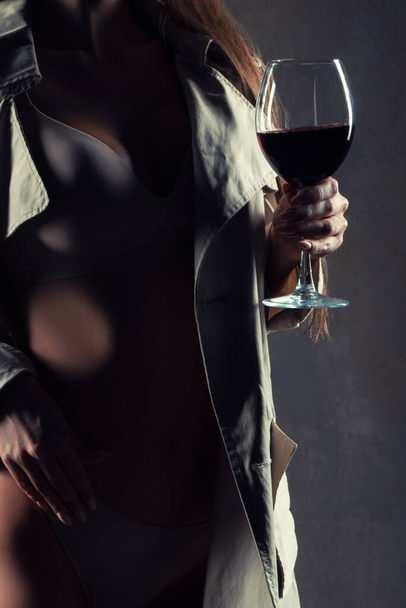 Rood wijnglas. jonge vrouw met een glas wijn, selectieve focus. Sexy vrouw dragen lingerie en jas - Foto, afbeelding