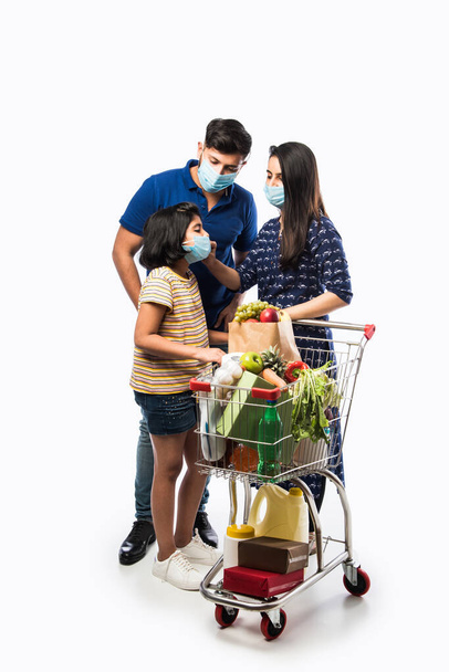 Indian Family Shopping with kids during virus outbreak. Mother, father and daughter wearing surgical face mask buying grocery in supermarket. Family in shop. - 写真・画像