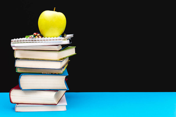 Manzana verde en la pila de libros y otros útiles escolares en la mesa azul contra pizarra. Concepto educativo. - Foto, imagen