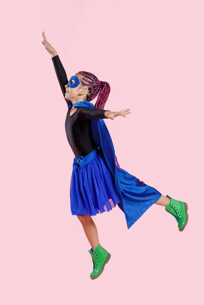 Klein meisje speelt superheld. Kind op de achtergrond van fel roze muur, dragen in kleurrijke kleren groene laarzen, roze haar. Meisjeskracht concept. - Foto, afbeelding
