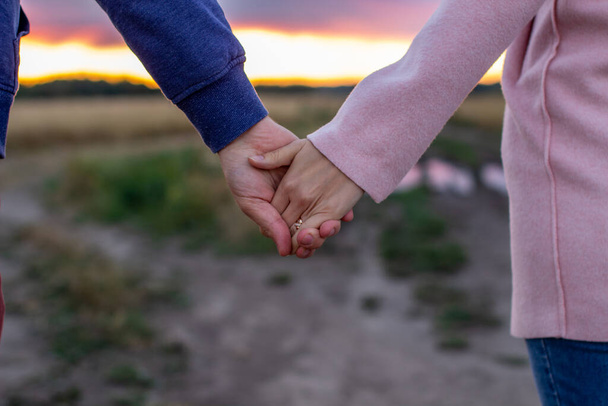 Sevgi dolu genç bir çift el ele tutuşuyor. Bir kızın elleri ve bir erkeğin yakın çekimi. Bir randevuda erkek ve kız doğada. - Fotoğraf, Görsel
