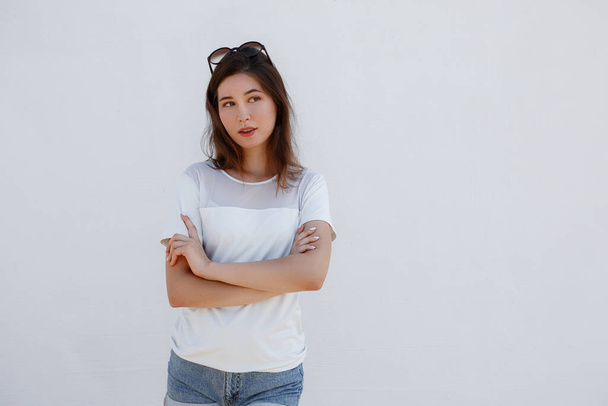Εικόνα μιας νεαρής Ασιάτισσας με λευκό πουκάμισο και ηλιοκαμένη πόζα απομονωμένη σε φόντο λευκού τοίχου. - Φωτογραφία, εικόνα