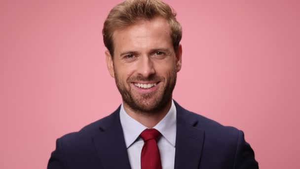 happy young businessman in navy blue suit smiling and showing piggy bank and house model, nodding and agreeing on pink background - Footage, Video