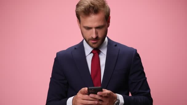 zszokowany młody biznesmen czytający e-maile, trzymający pięści w górze i wiwatujący, śmiejący się i wrzeszczący na różowym tle - Materiał filmowy, wideo