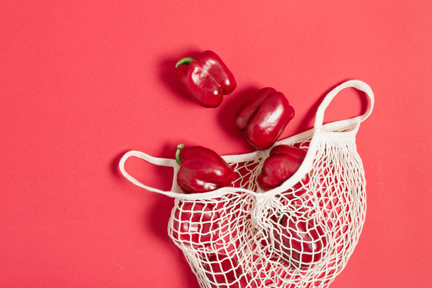 白いメッシュ再利用可能なショッピングバッグトップビューで赤ベルペッパー。エコショッピングのコンセプト。健康的な食事.  - 写真・画像