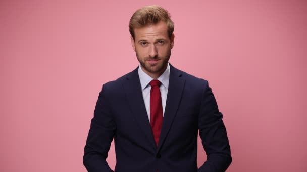 glücklicher junger Geschäftsmann im marineblauen Anzug, der aufblickt, lächelt und mit den Fingern auf rosa Hintergrund zeigt - Filmmaterial, Video