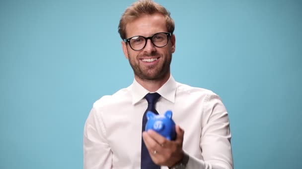 liikemies laittaa rahansa säästöpossu kun heiluttaa nyrkkiä ja juhlii menestystä sinisellä pohjalla - Materiaali, video