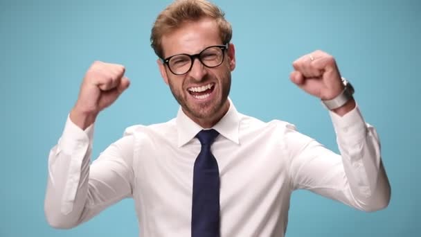 excited businessman waving his fists in the air and celebrating succes on blue background - Footage, Video