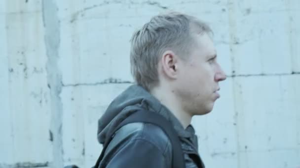 giovane uomo caucasico pensoso in giacca nera con cappuccio passeggiando lungo la parete - Filmati, video