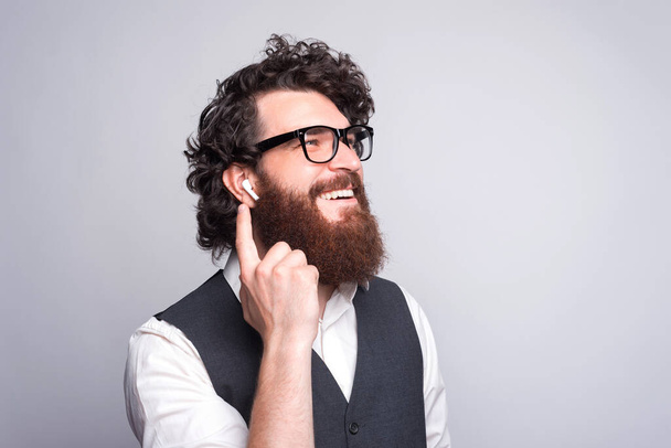 Крупный план портрета бородатого человека в костюме, улыбающегося и использующего наушники. - Фото, изображение