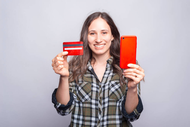 Zdjęcie młodej uśmiechniętej kobiety z czerwoną kartą kredytową i smartfonem - Zdjęcie, obraz