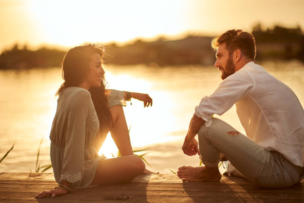 Young couple in emotional chatting on the sunset on the shore of the lake - Photo, image