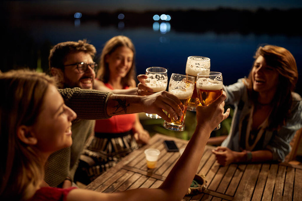 Group of friends having a toast wit the beer in the bar on the lake with a beautiful night - Foto, Bild