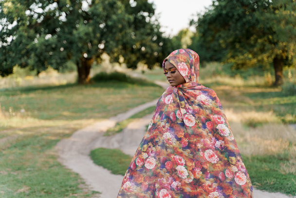 Stílusos vonzó muszlim lány divatos hagyományos ruhákban, nő hagyományos hidzsáb csukott szemmel. Az egész világ kultúrái. Afrikai emberek életmódja a zöld mezőn. - Fotó, kép