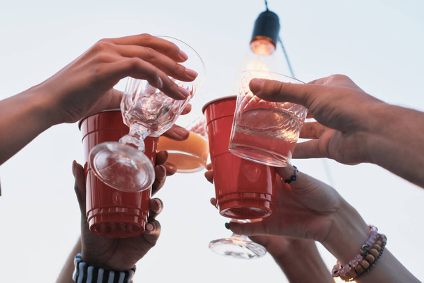 Nahaufnahme einer Gruppe von Menschen, die mit einem Glas Cocktail anstoßen und im Freien feiern - Foto, Bild