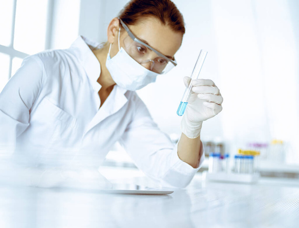 Laborassistentin analysiert Reagenzglas mit blauer Flüssigkeit. Medizin, Gesundheitswesen und Forschungskonzept - Foto, Bild