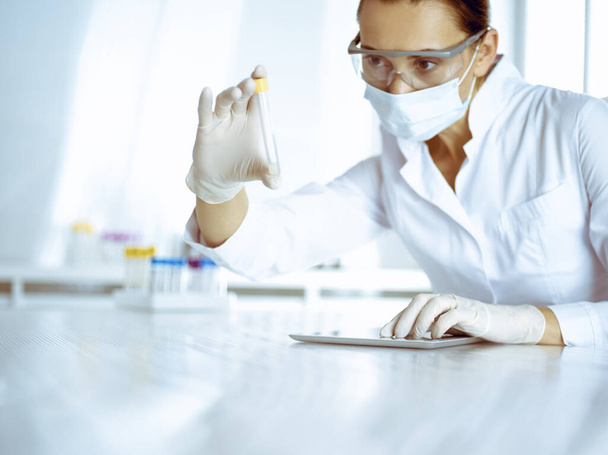 Female laboratory assistant analyzing a blood sample at hospital. Medicine, health care and researching concept - Foto, Imagem