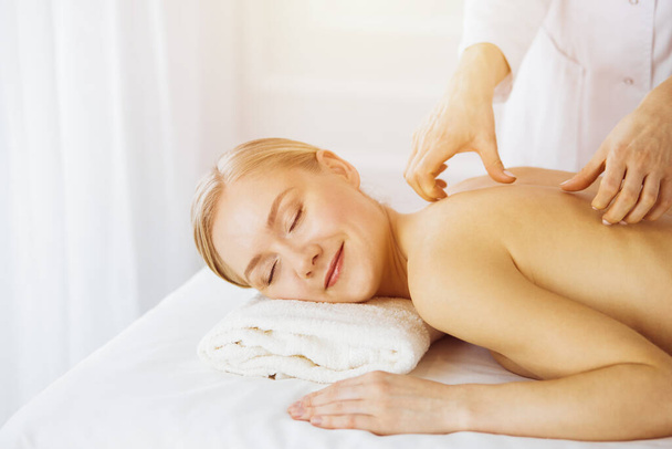 Beautiful caucasian woman enjoying back massage sunny spa salon. Beauty concept - Фото, зображення