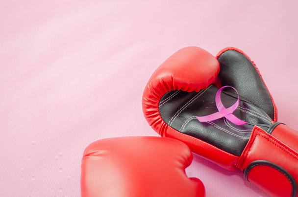 Pink ribbon placed on the boxing gloves.Red boxing gloves placed on a pink background.Do not focus on objects.World Breast Cancer Day Concept. - Photo, image