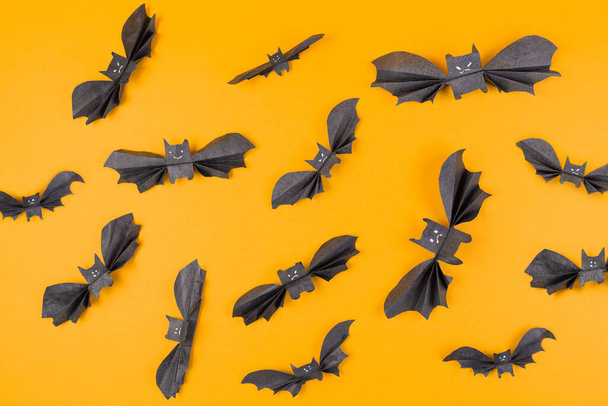 Mnoho netopýrů vyrobených z papíru na oranžovém pozadí. Ležel. Koncept Halloweenu a sváteční dekorace. - Fotografie, Obrázek