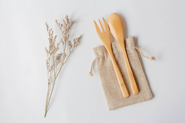 Επίπεδη στρώση βιώσιμων προϊόντων, ξύλινη κουτάλα με φυσικό σάκο και στεγνά λουλούδια σε λευκό φόντο.. - Φωτογραφία, εικόνα