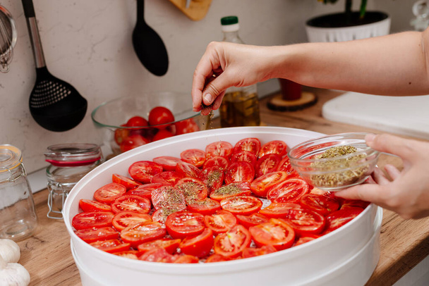 Sun-dried tomatoes. The process of cooking sun-dried tomatoes. The woman is preparing tomatoes in the kitchen. A woman cuts tomatoes, greases them with oil and spices them.  - Foto, Imagem