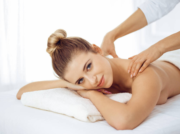 Young and blonde woman enjoying massage of back in spa salon. Beauty concept - Fotografie, Obrázek
