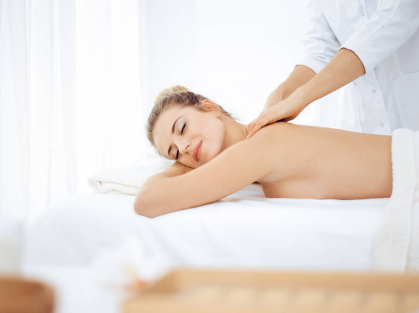 Young and blonde woman enjoying massage of back in spa salon. Beauty concept - Foto, imagen