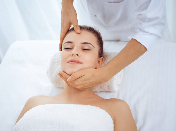 Young and blonde woman enjoying facial massage in spa salon. Beauty concept - Фото, зображення