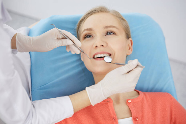 Smiling caucasian woman is being examined by dentist at dental clinic. Healthy teeth and medicine, stomatology concept - Foto, Bild